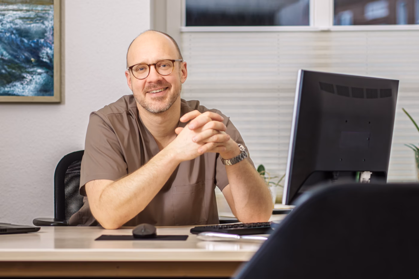 Dr. med. Reitz sitzt lächelnd an seinem Schreibtisch in der Praxis